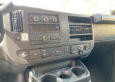 The image shows the dashboard of a vehicle, featuring climate controls, a radio, various buttons and switches, air vents, cup holders, and a section with two 12V power outlets. The dashboard is mostly black.